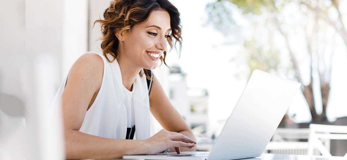 Smiling woman sitting at a table and typing on a laptop.