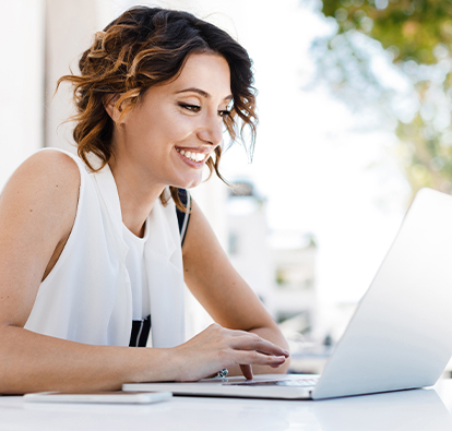 Smiling woman sitting at a table and typing on a laptop.