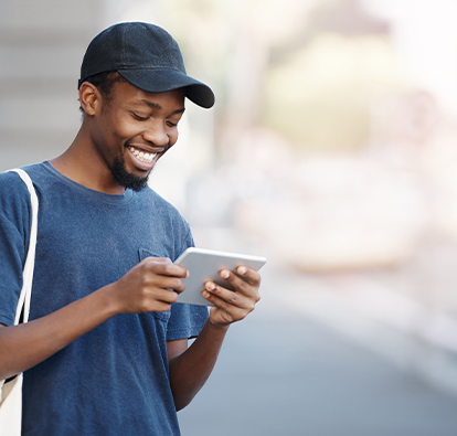 Man with baseball cap, smiling and looking at a mobile device.